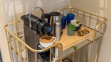 Una máquina de café sobre un carrito con una taza de café, una termo y una pequeña planta.