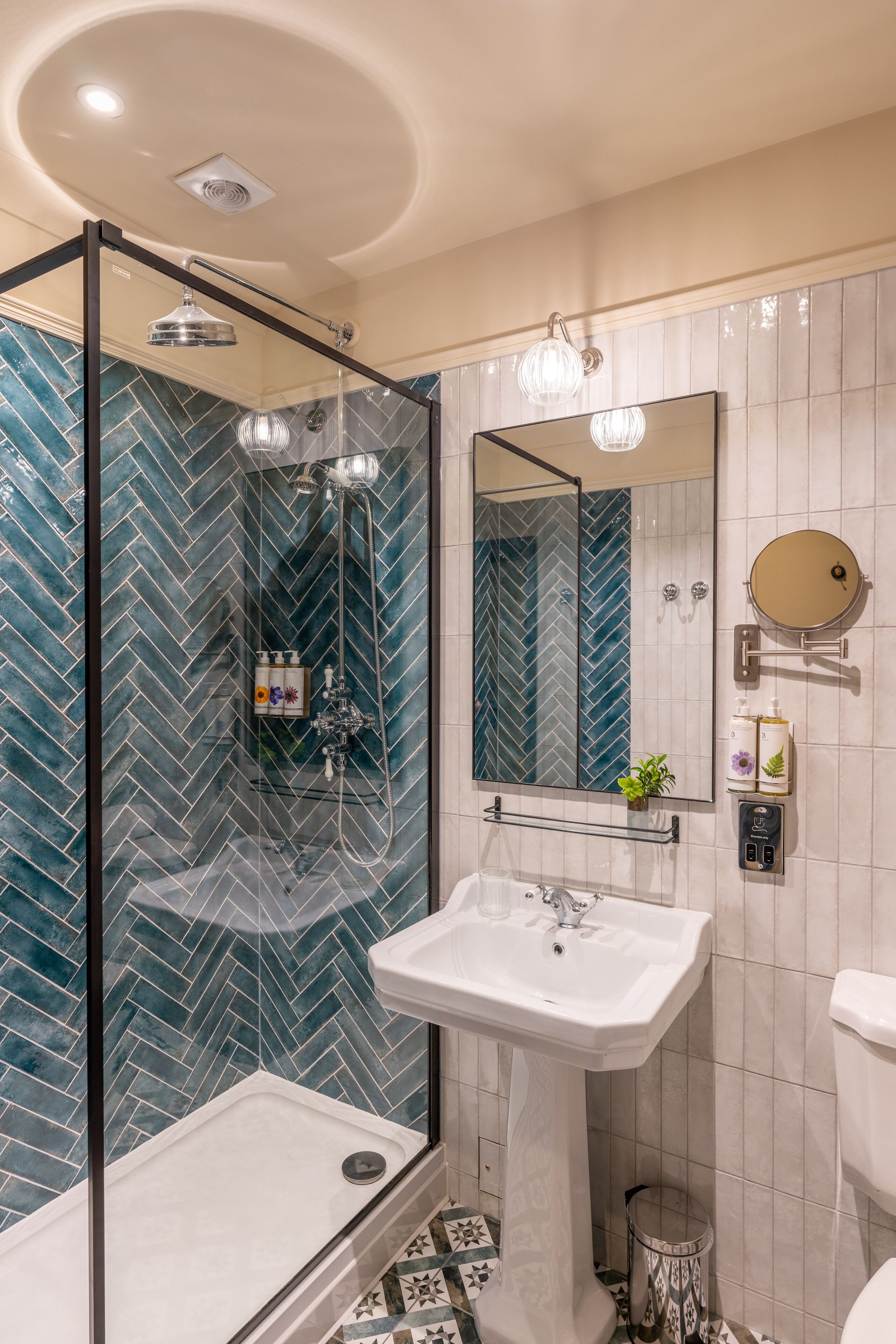 Un baño moderno con ducha de vidrio, lavamanos blanco y un espejo grande.