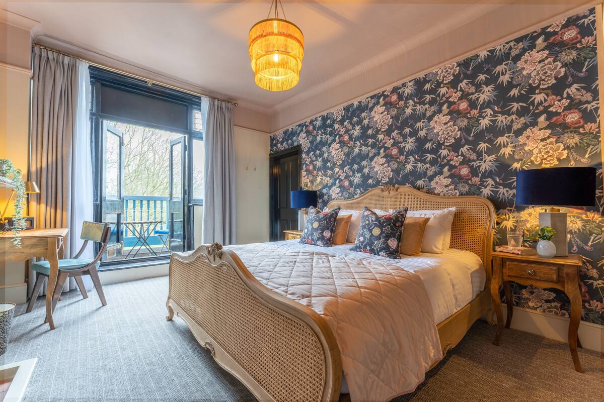 Une chambre avec un grand lit, un bureau et une chaise. Il y a une fenêtre avec des rideaux et une vue sur l’extérieur.