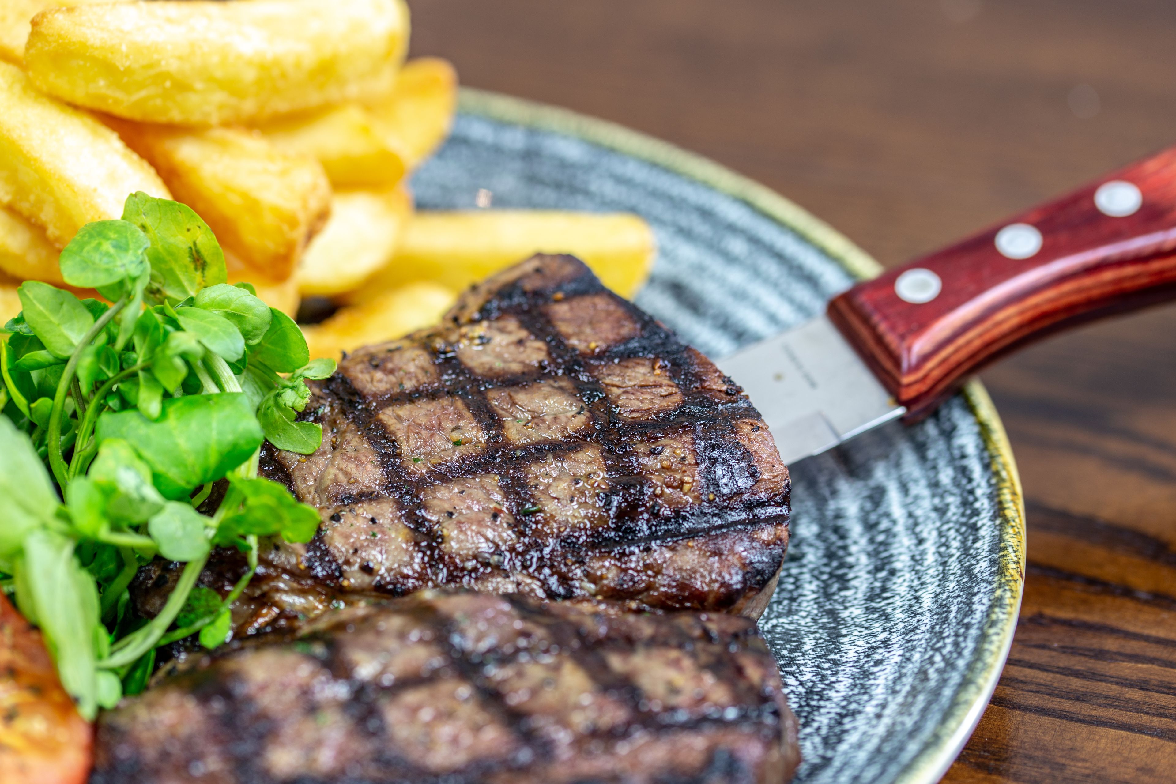 A plate with grilled steak, fries, and greens.