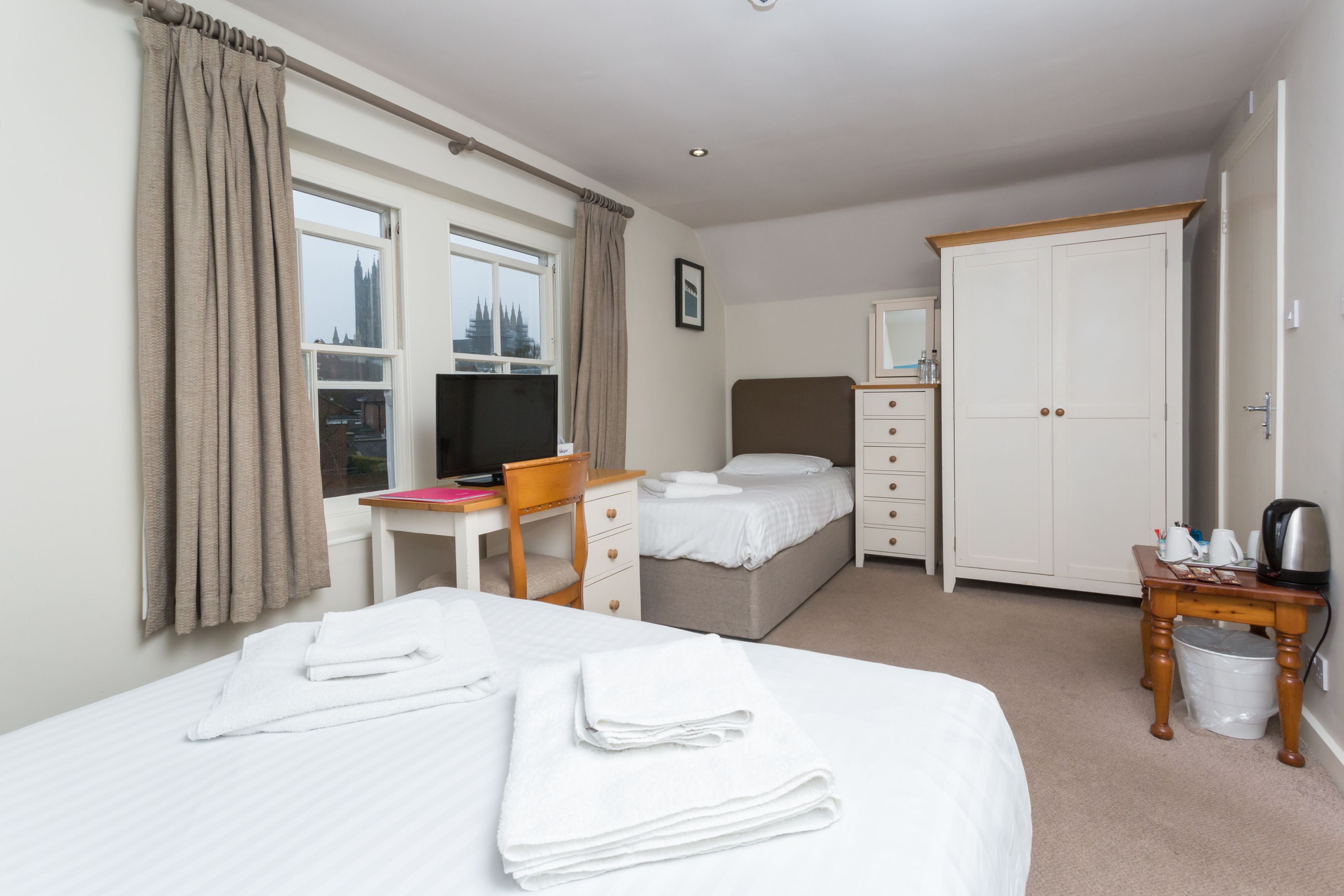 Una habitación de hotel con cama, escritorio, armario y ventana con cortinas.