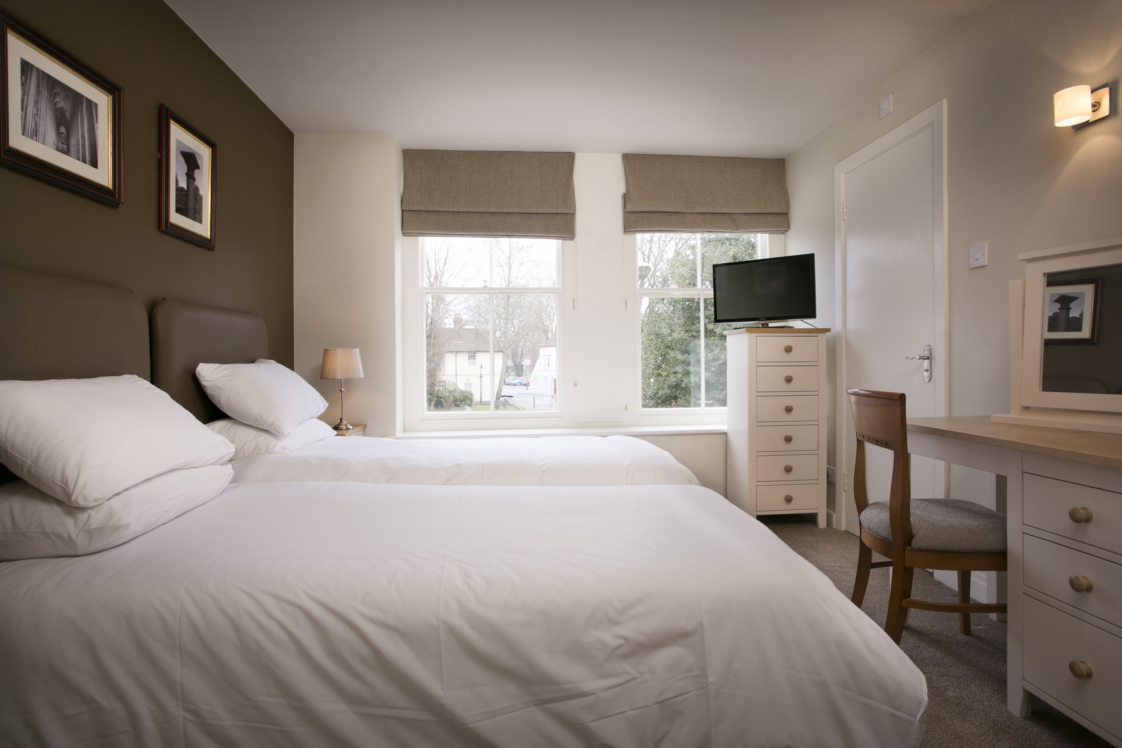 Ein Schlafzimmer mit zwei Betten, einem Schminktisch, einem Fernseher und einem Fenster mit Vorhängen.