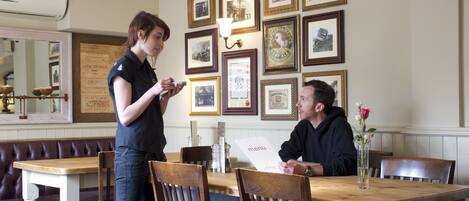 A restaurant with wooden tables and chairs, framed pictures on the wall, and a menu on the table.