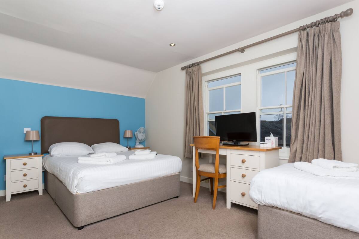A hotel room with a large bed, a desk with a chair, a TV, and a window with curtains.