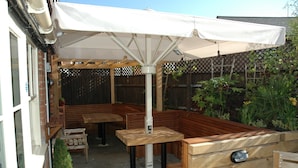 An outdoor patio with wooden benches and tables, a white umbrella, and a wooden fence. - The Millers Arms (Canterbury)