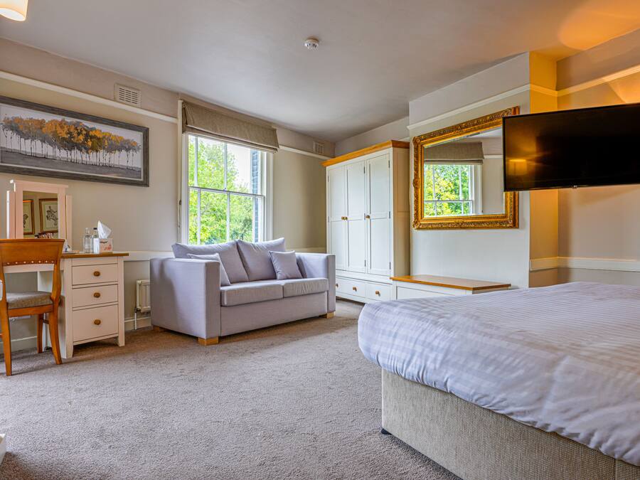A bedroom with a bed, a desk, a chair, a sofa, a wardrobe, and a TV.
