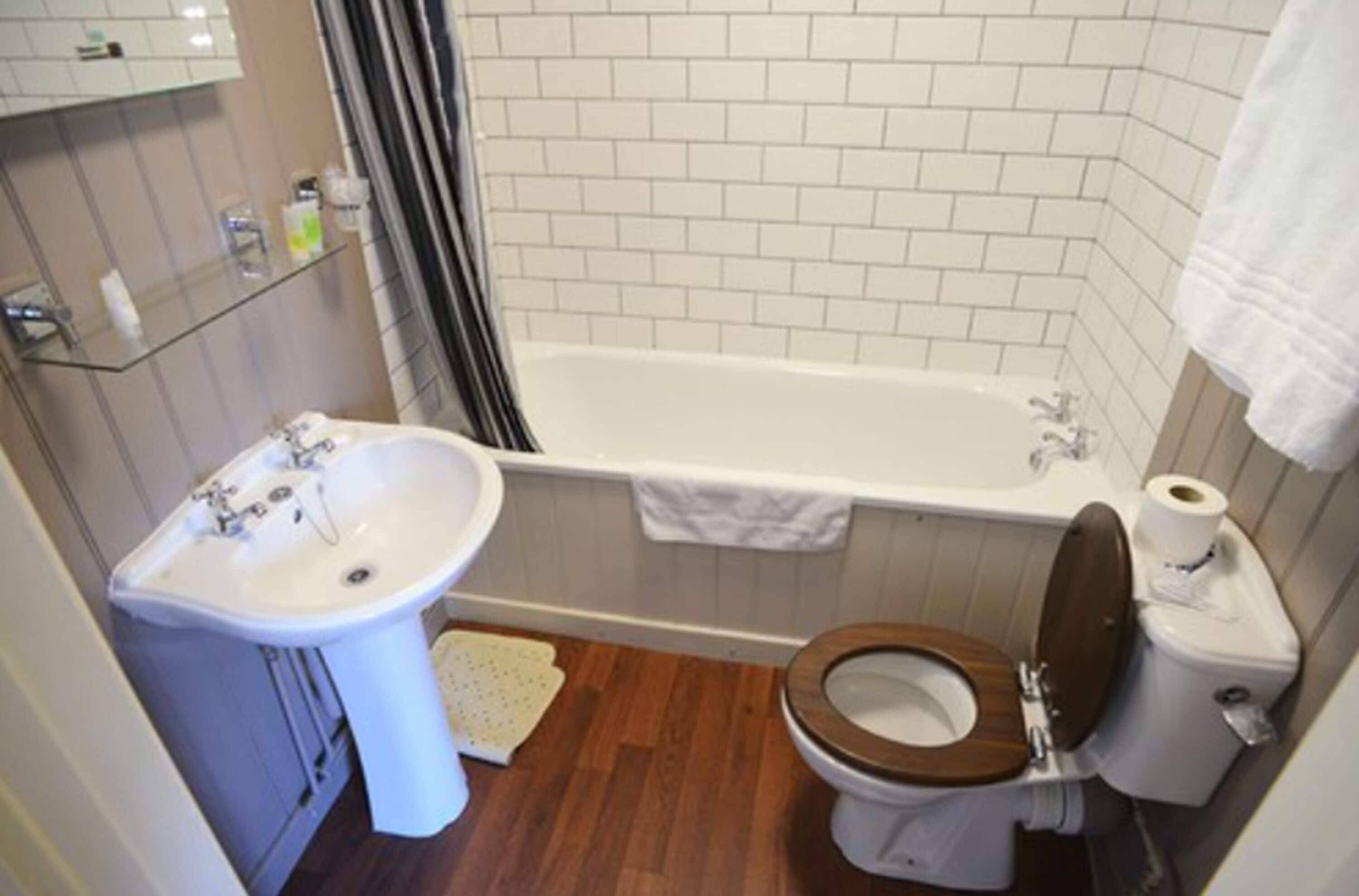 A bathroom with a white sink, a wooden toilet, a bathtub, and a shower curtain.