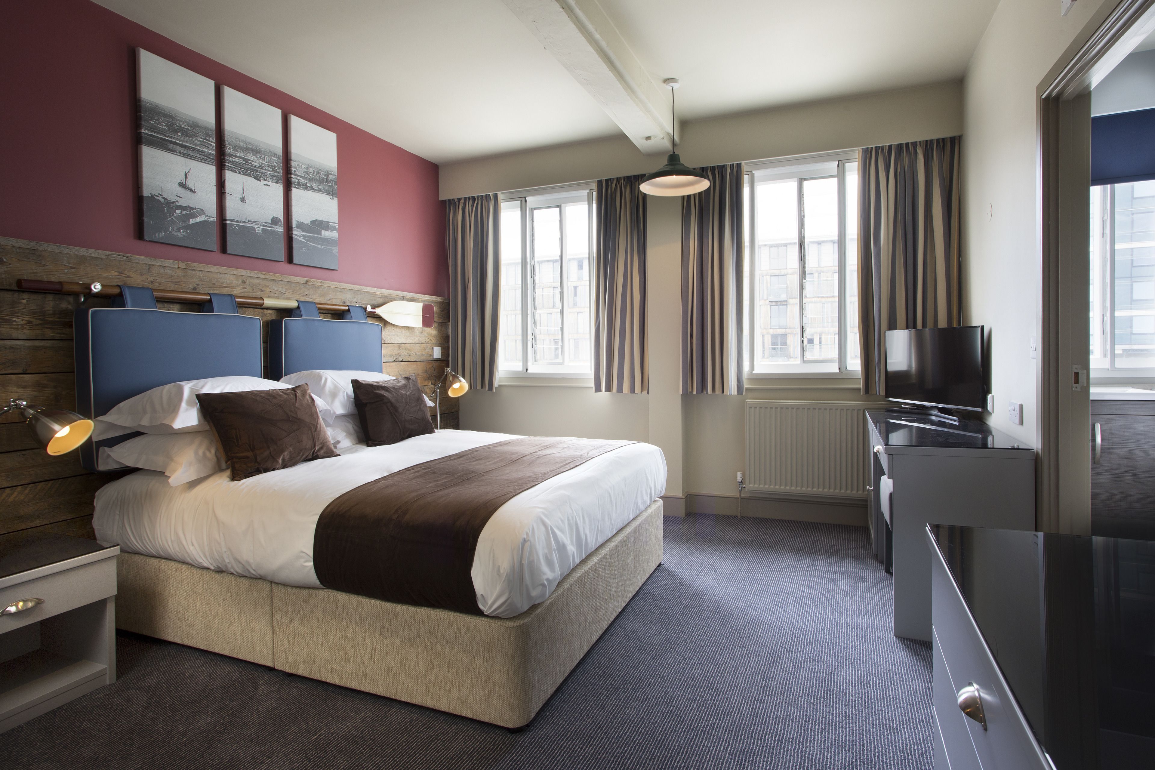 A modern hotel room with a large bed, a television, and a view of the city through large windows.