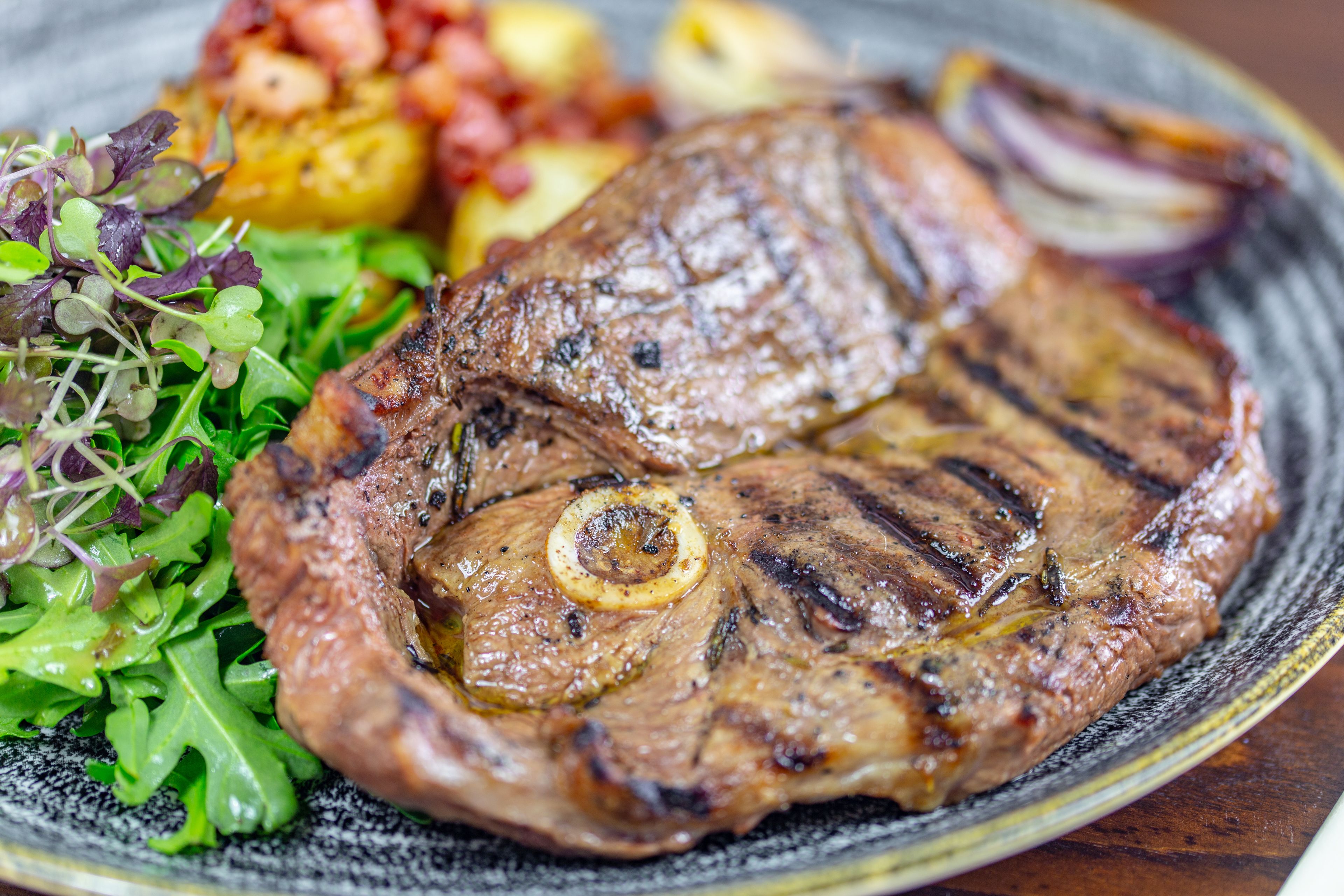 A steak with grill marks, accompanied by roasted potatoes and a side salad.