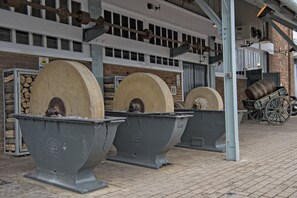 Stora, industriellt utformade blomkrukor med metallfötter, en byggnad i tegel med fönster och en träkärra i bakgrunden.
