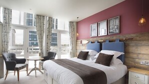 A hotel room with a large bed, a chair, a small table, and a nightstand.