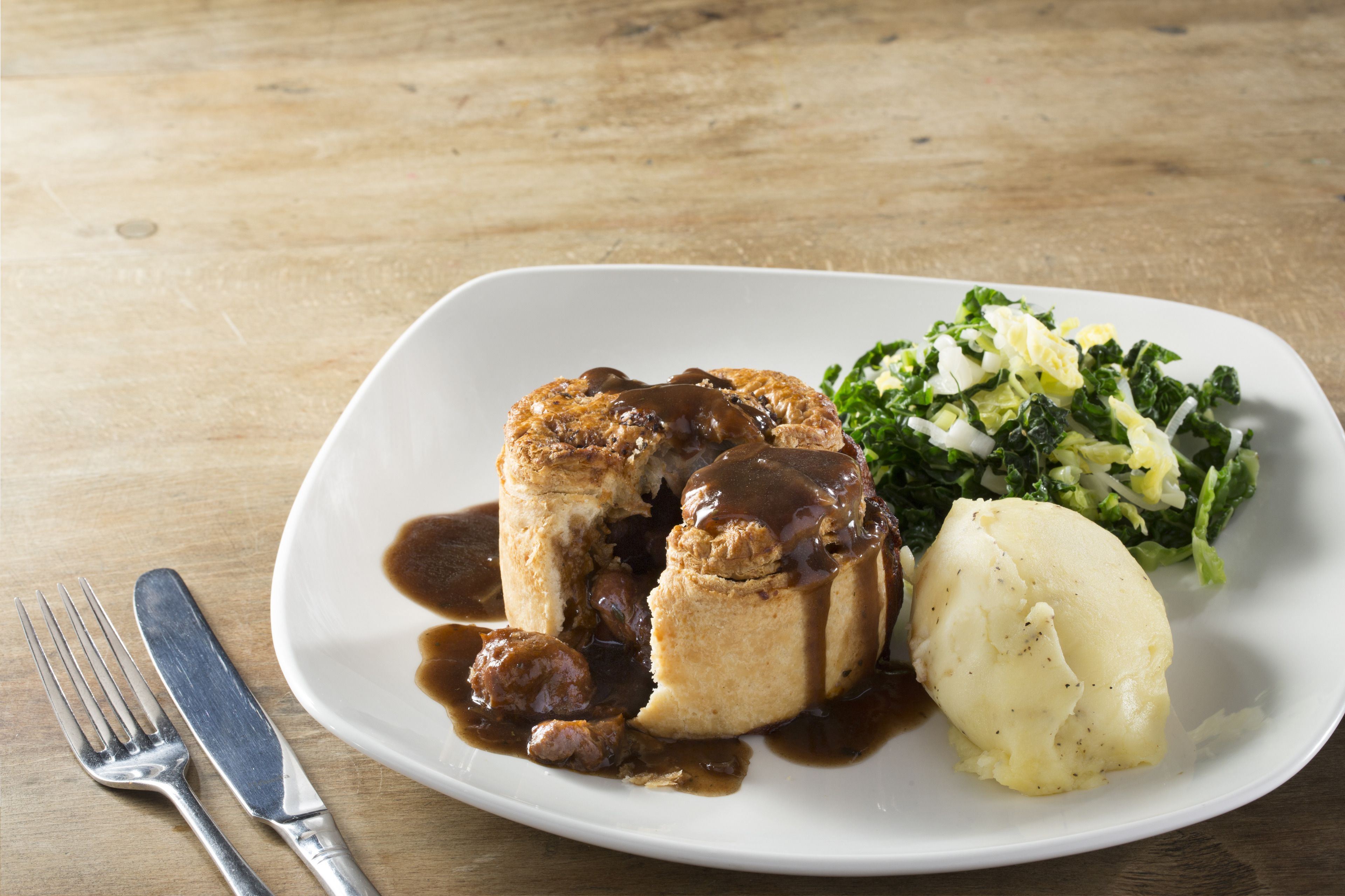 A plate with a meat dish, mashed potatoes, and a side salad on a wooden table.