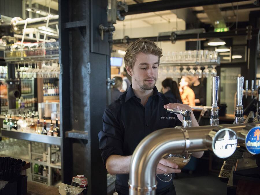 A bartender at a bar with multiple taps and shelves of bottles in the background.
