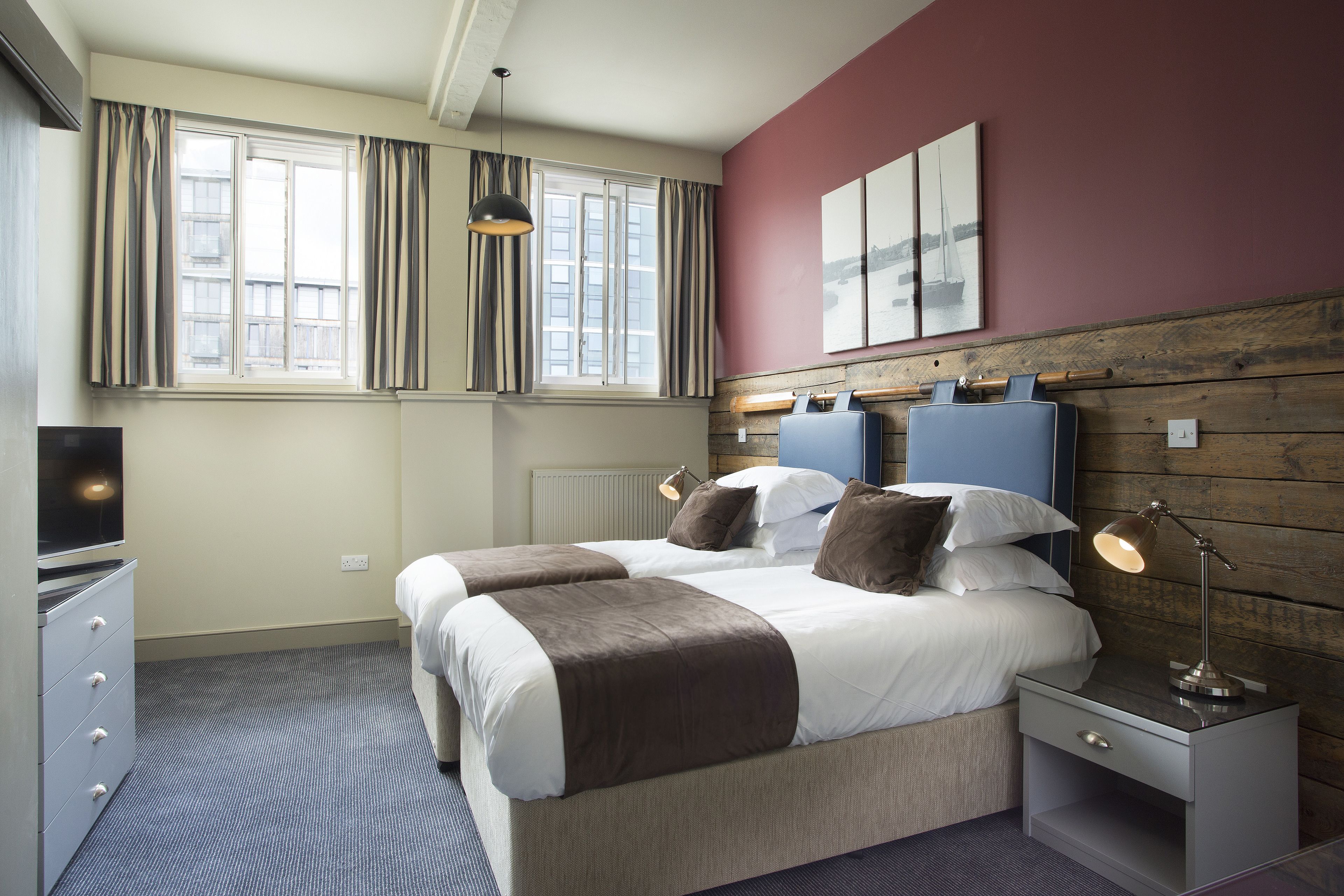 Een hotelkamer met een groot bed, een nachtkastje met een lamp, een kast en een raam met gordijnen.