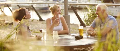 Three people sitting at an outdoor table with drinks, overlooking a marina with boats.