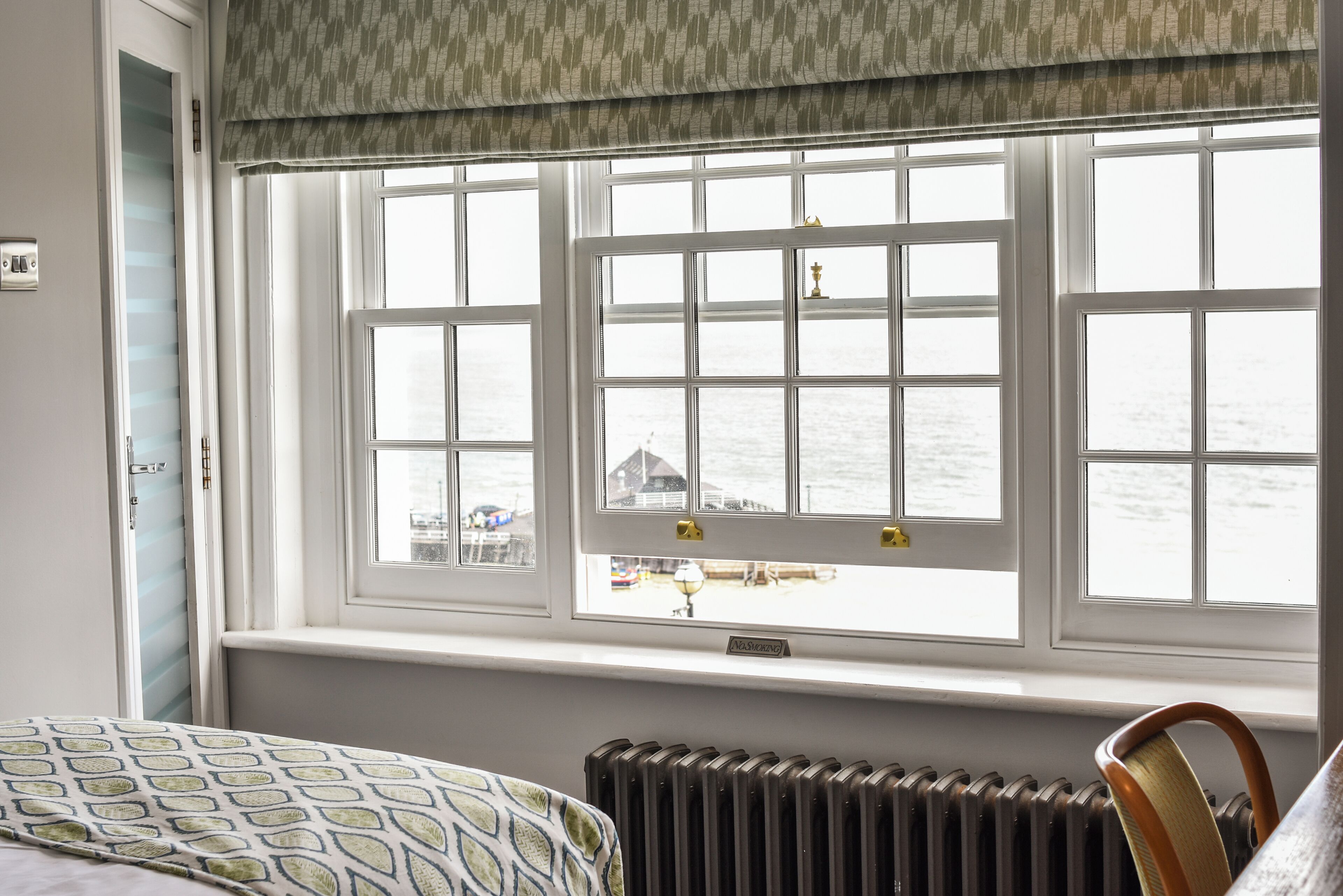 A room with a bed, a radiator, and a window with a view of the sea.