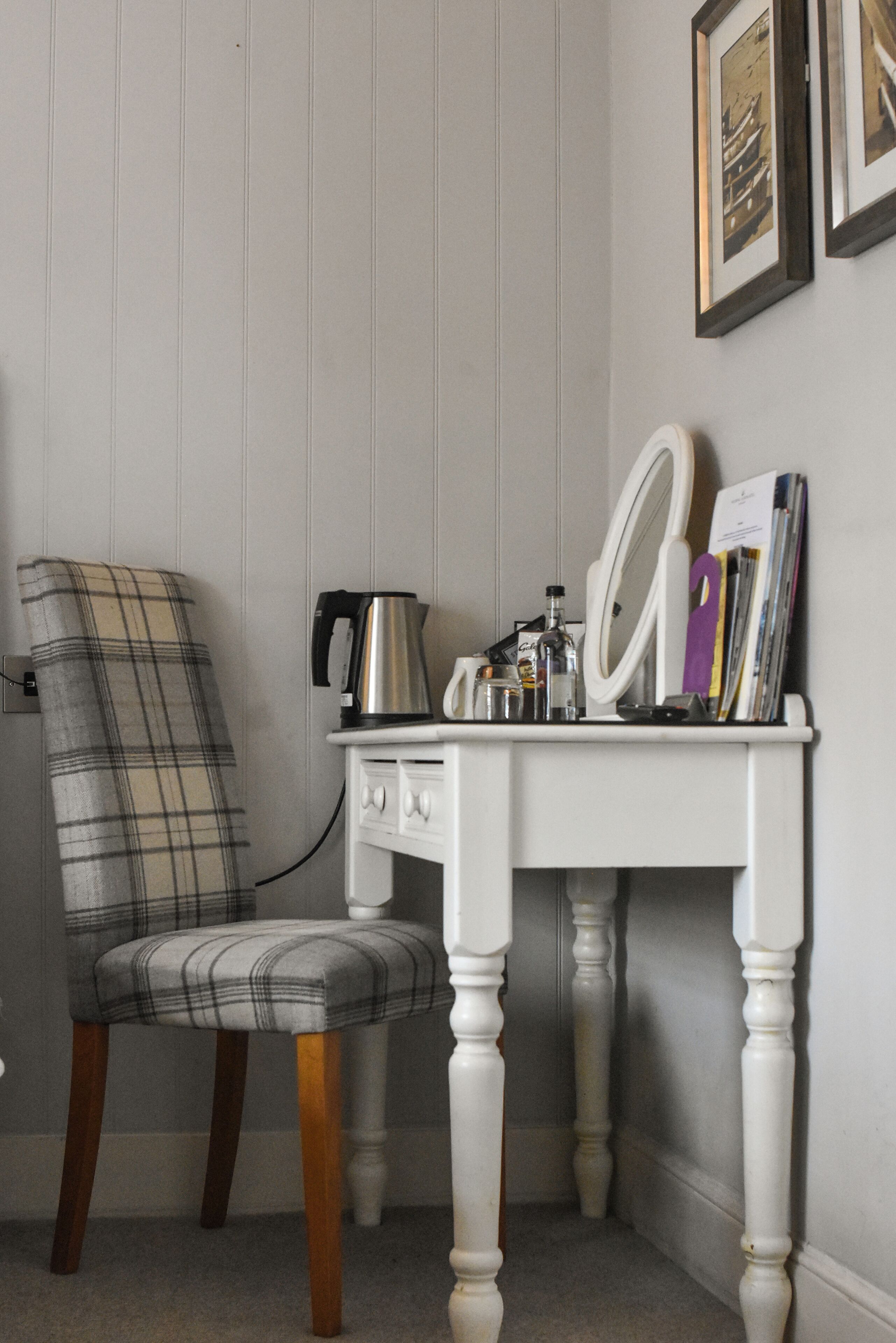 A corner room with a plaid chair, a white dresser with a mirror, and a kettle.