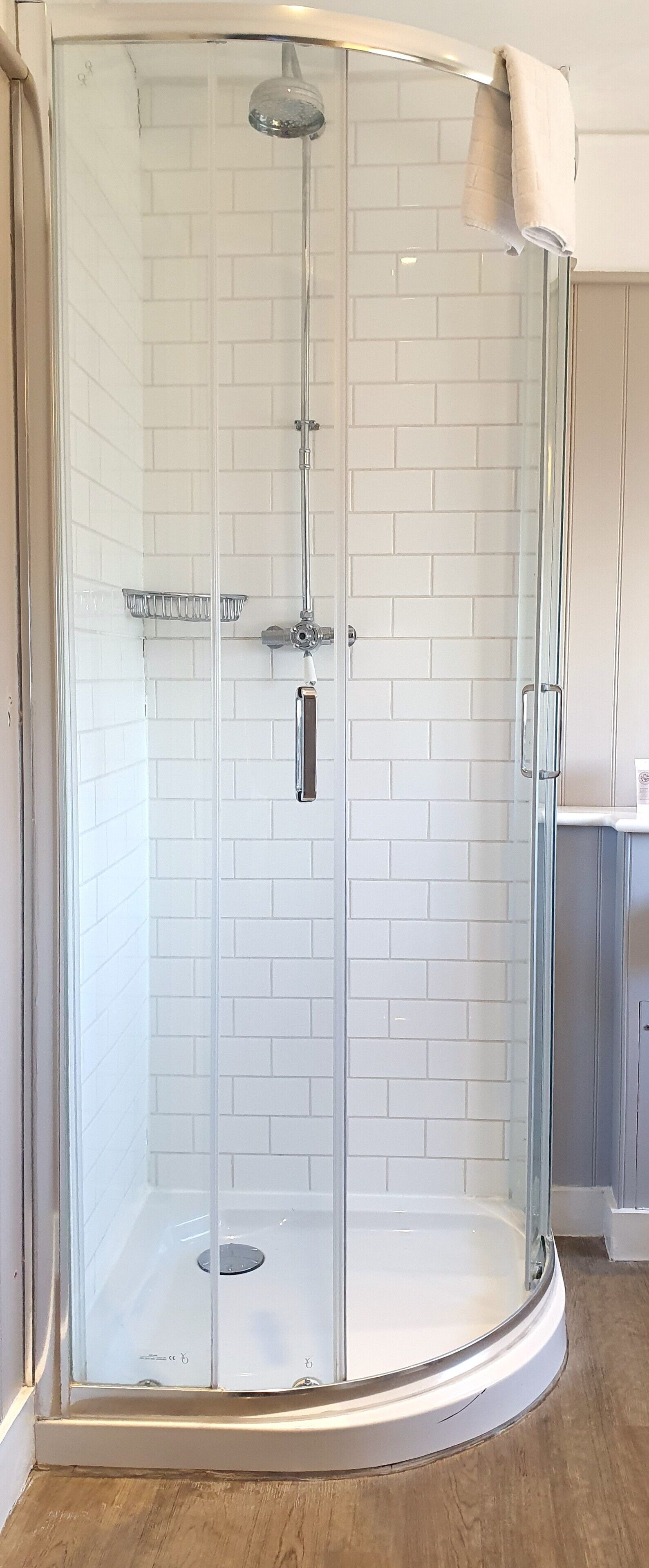 A glass-enclosed shower with a white tiled wall, a showerhead, and a towel rack.