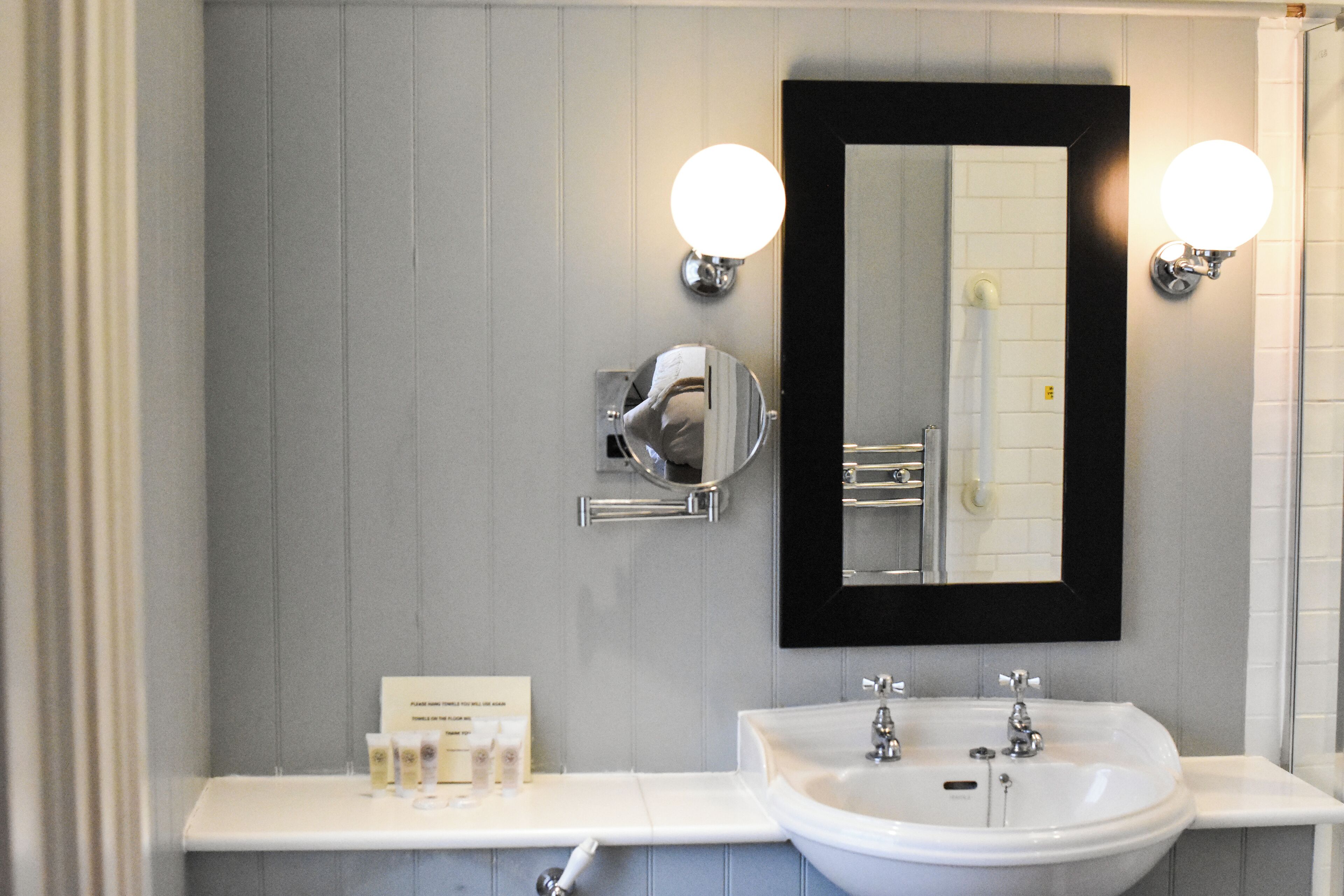 A bathroom with a white sink, two wall-mounted lights, a mirror, and a towel rack.