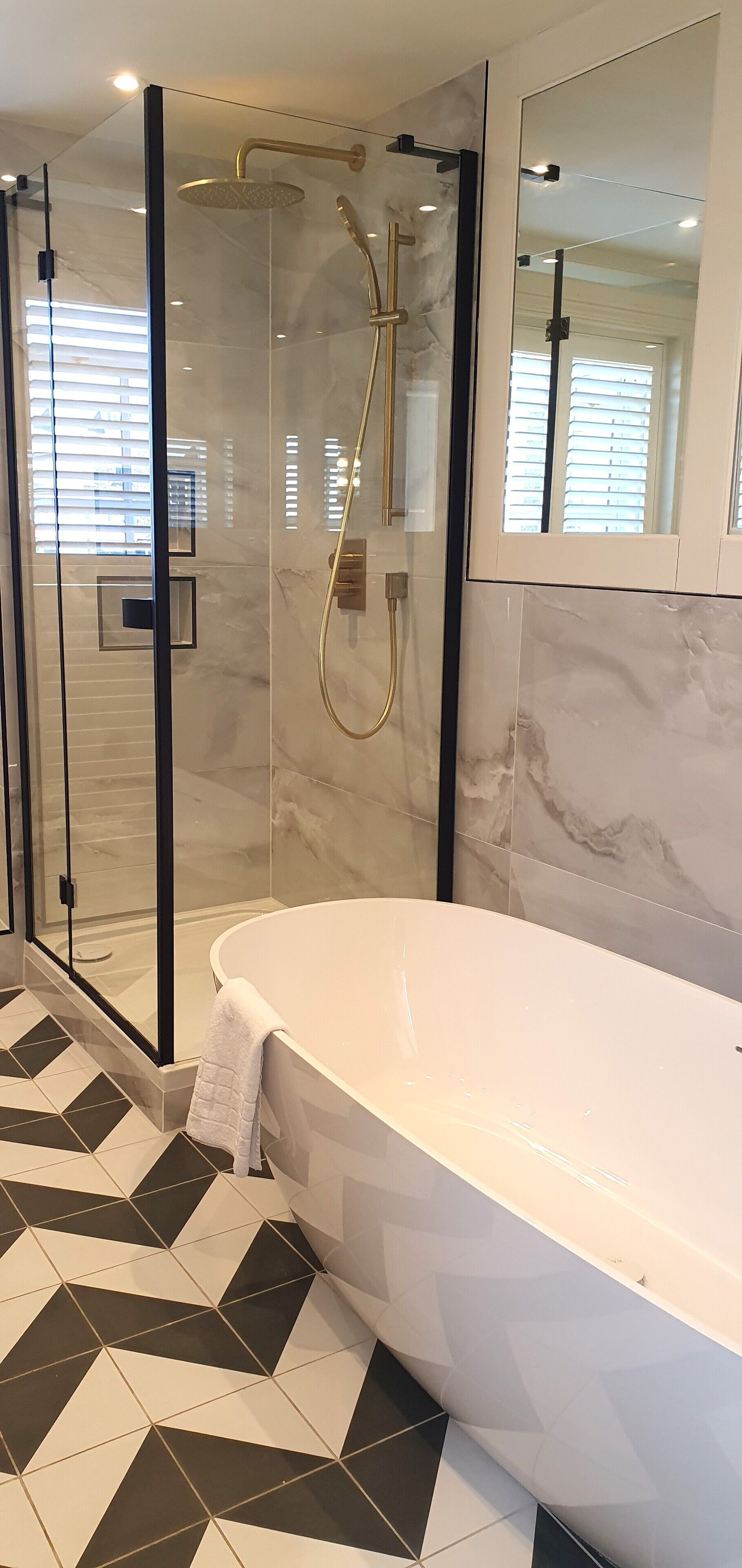 Un baño moderno con una bañera independiente, ducha con cerramiento de vidrio y suelo con estampado geométrico.