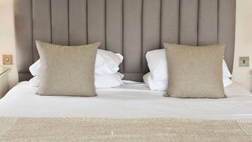 Una cama bien tendida con cabecera, dos almohadas y un tapete texturizado.