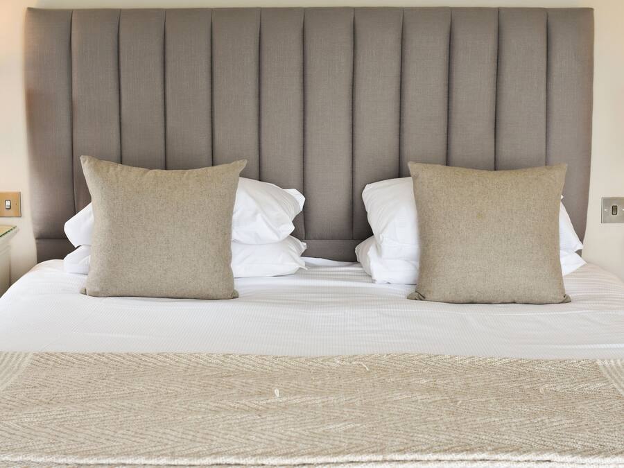 Una cama bien tendida con cabecera, dos almohadas y un tapete texturizado.