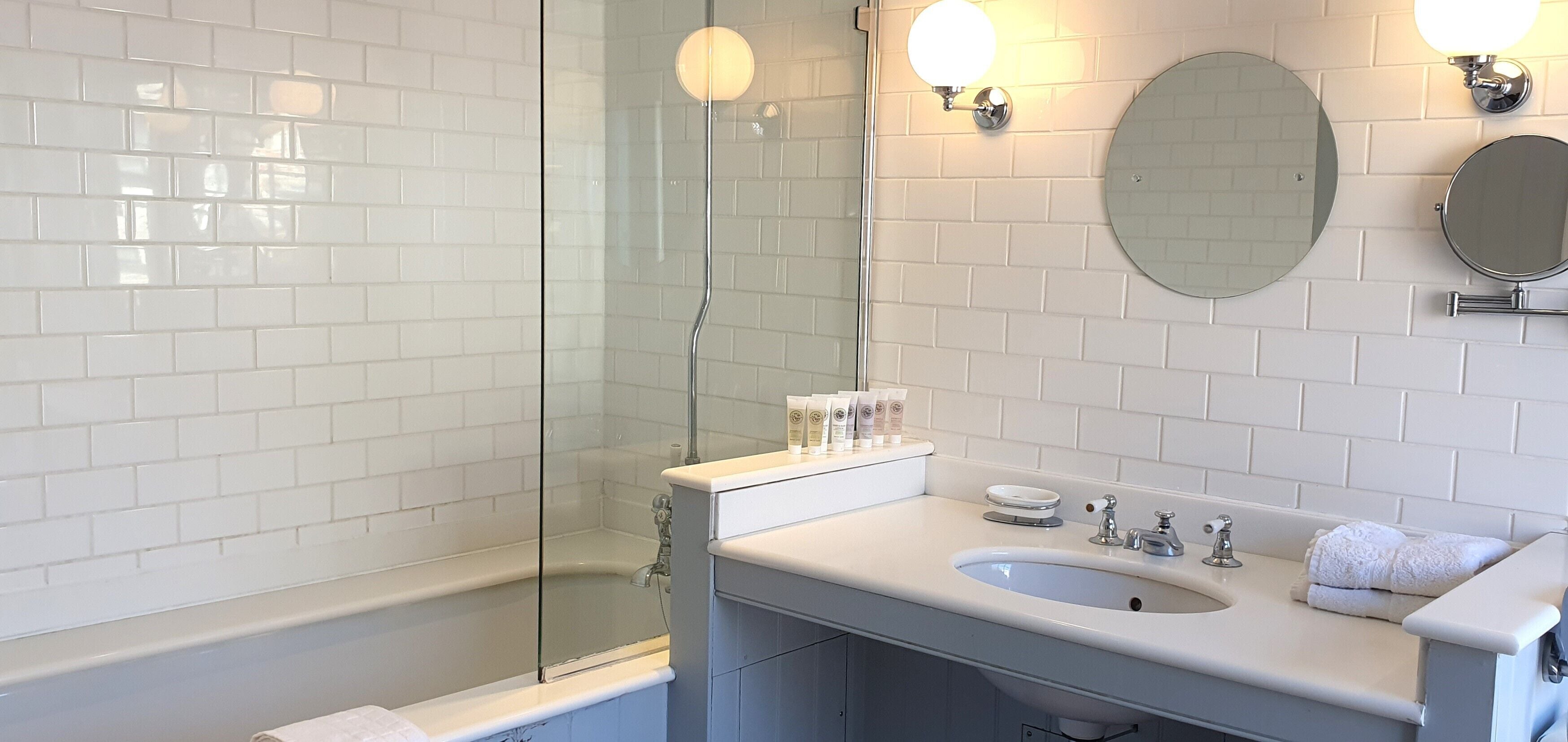 Ein modernes Badezimmer mit einer gläsernen Dusche, einem weißen Waschbecken mit zwei Wasserhähnen und einem Spiegel darüber.