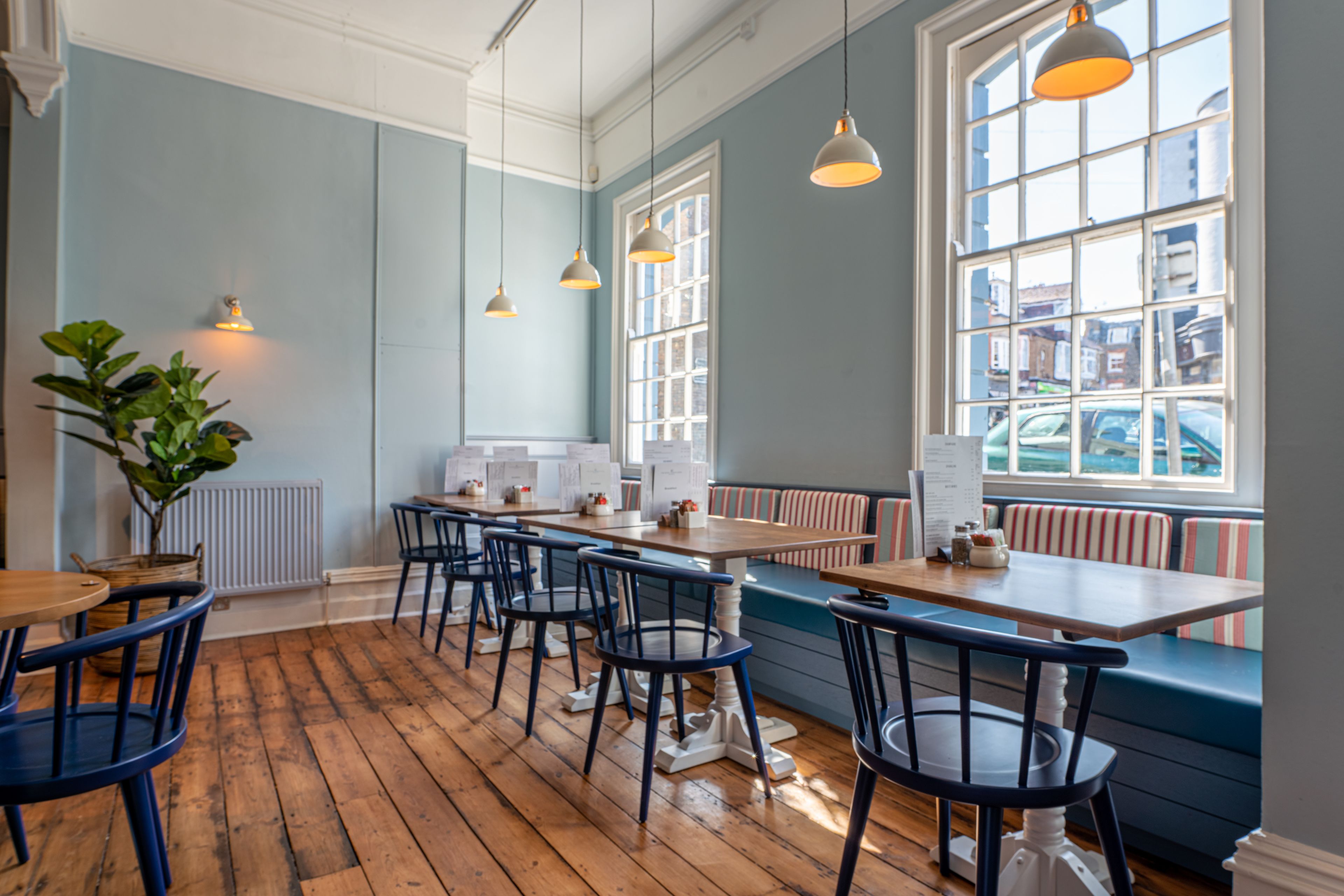 Un restaurante con suelos de madera, paredes azules y vistas a la ciudad a través de amplios ventanales.