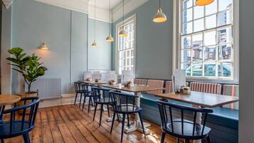 Un restaurante con suelos de madera, paredes azules y vistas a la ciudad a través de amplios ventanales.
