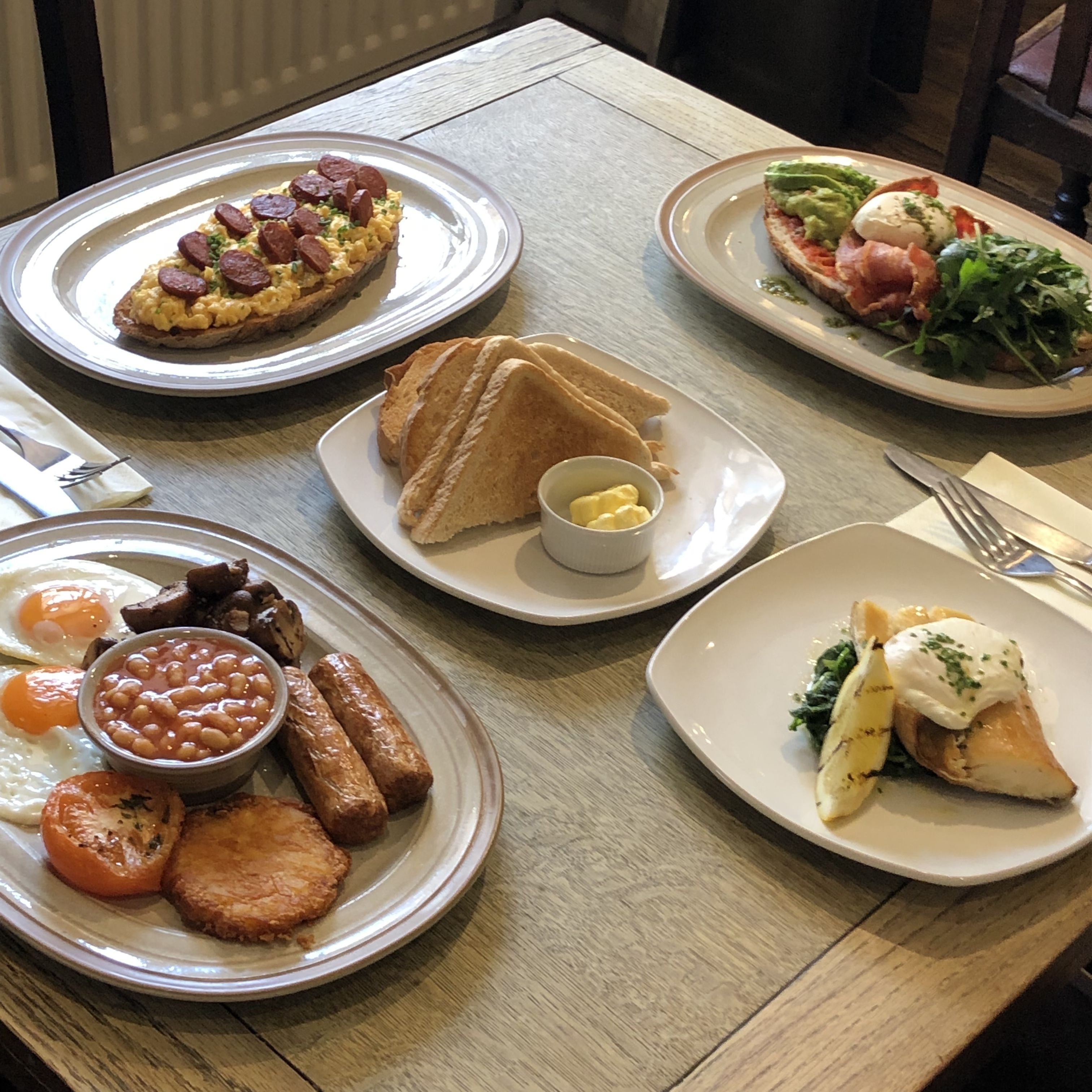 Una mesa con diversos platos, entre ellos huevos, salchichas, tostadas y ensaladas.