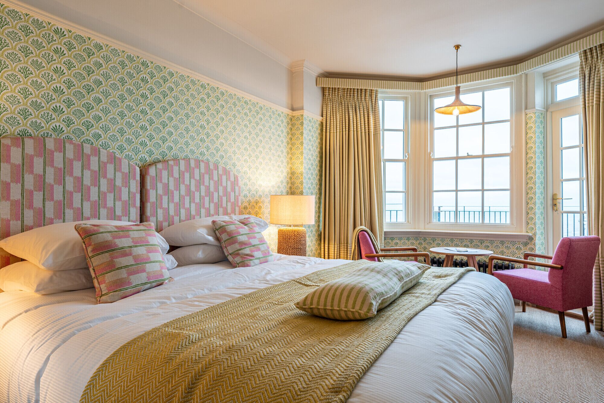 A hotel room with a large bed, a small table, a chair, and a window with curtains.