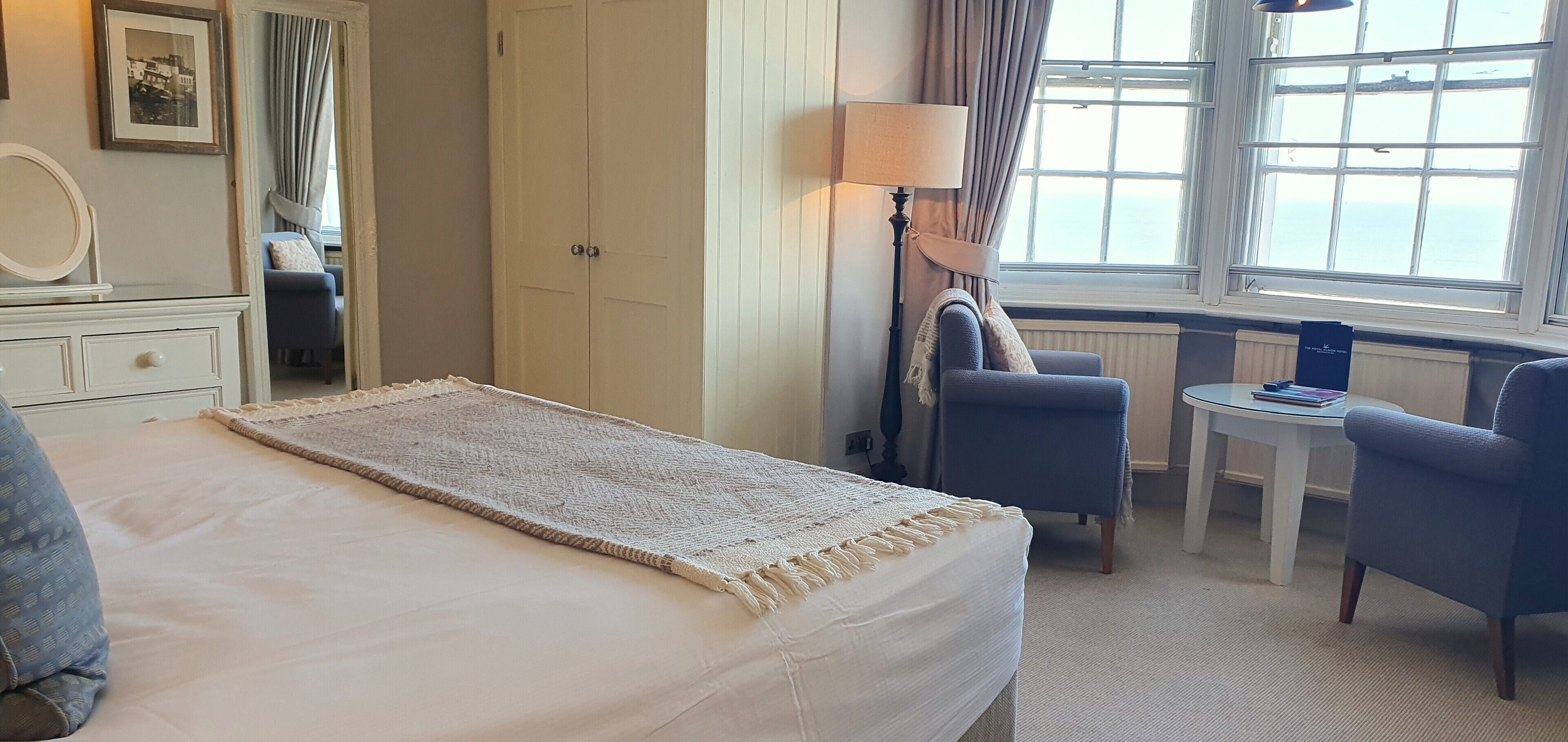 A hotel room with a bed, a desk, two chairs, a lamp, a window with a view, and a wardrobe.