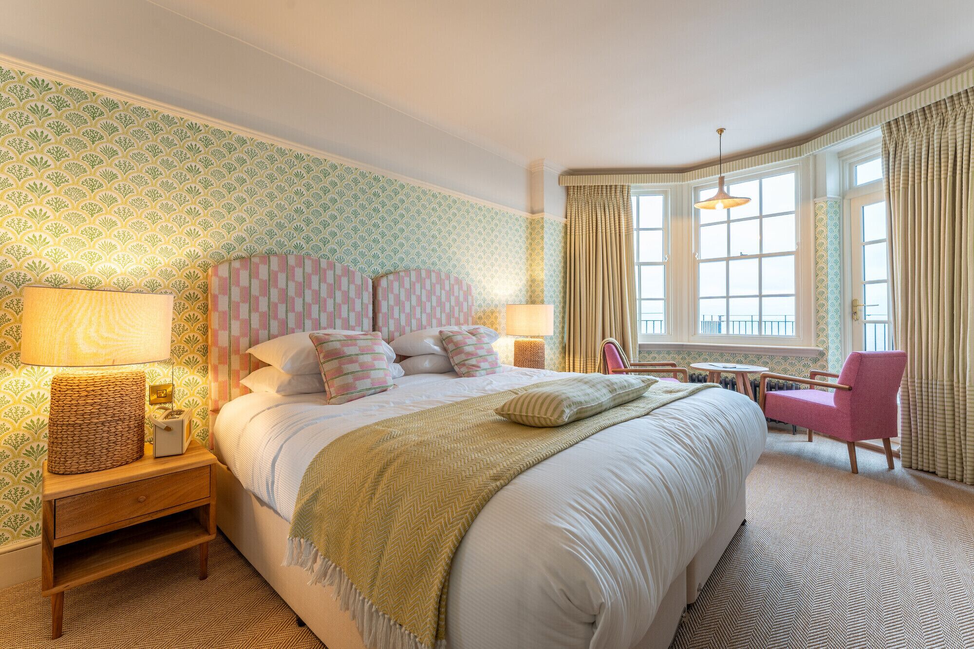 Une chambre d’hôtel avec un grand lit, une table de chevet avec une lampe, une chaise et une fenêtre avec des rideaux.