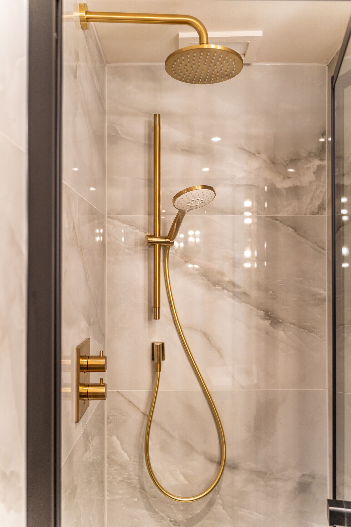 Eine moderne Dusche mit einer goldfarbenen Duschbrause und einem Duschschlauch, vor einer Marmorwand.