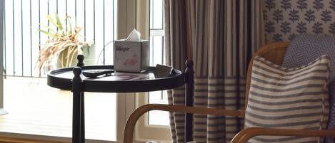 A room with a wicker chair, a small table with a tissue box, striped curtains, and a patterned wall.