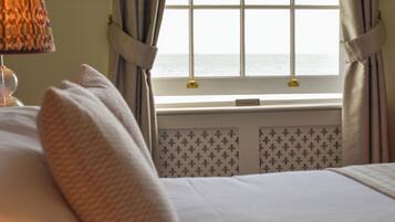 A neatly made bed with a pillow, a lamp on a bedside table, and a window with curtains.