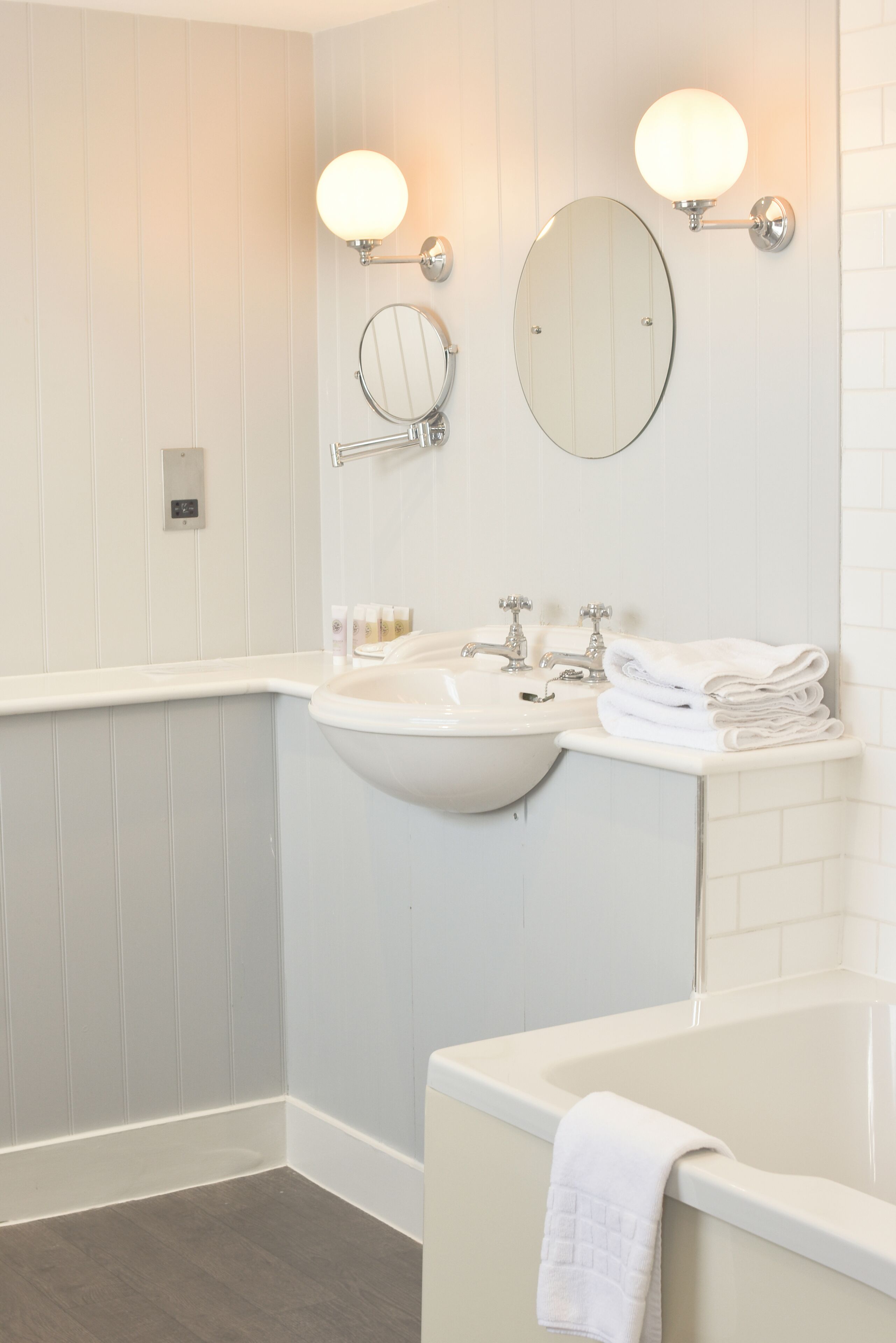 Ein Badezimmer mit einem Waschbecken, zwei Spiegeln an der Wand, einer Badewanne und einem Stapel Handtücher.