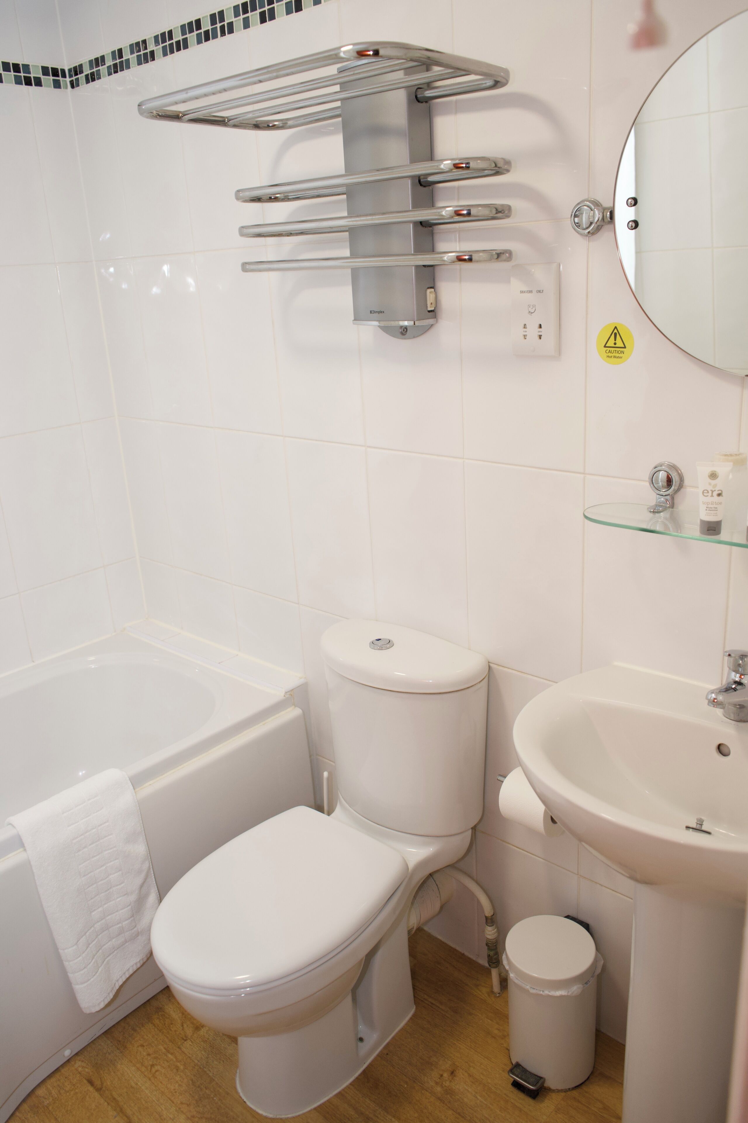 Een badkamer met een wit toilet, een bad, een wastafel en een glazen plank met toiletartikelen.