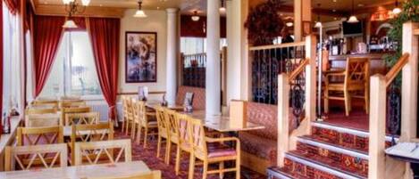 A restaurant with wooden tables and chairs, a staircase with a patterned carpet, and hanging lights.