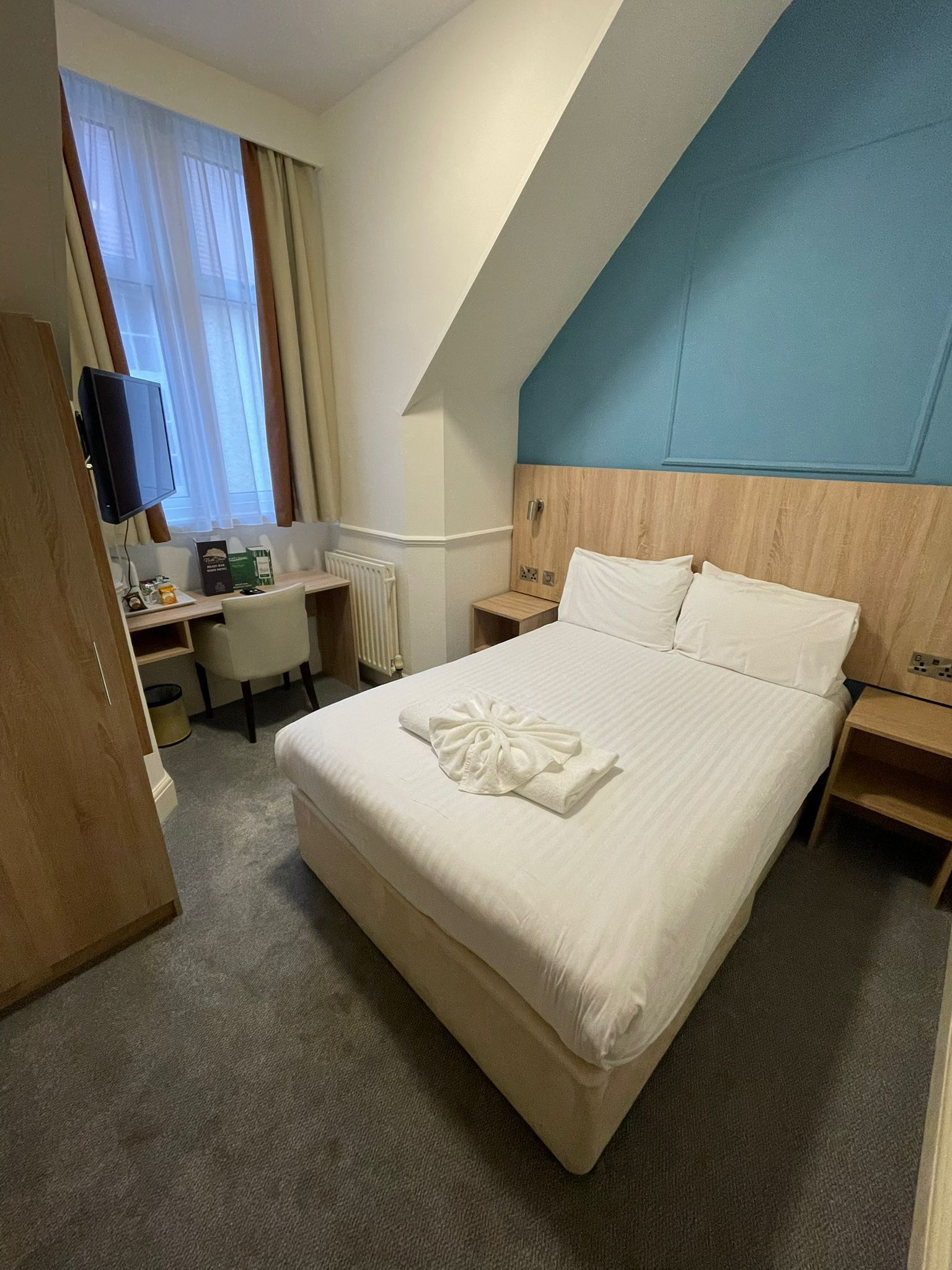 Ett hotellrum med en stor säng, ett skrivbord, en stol, en tv och ett fönster med gardiner.