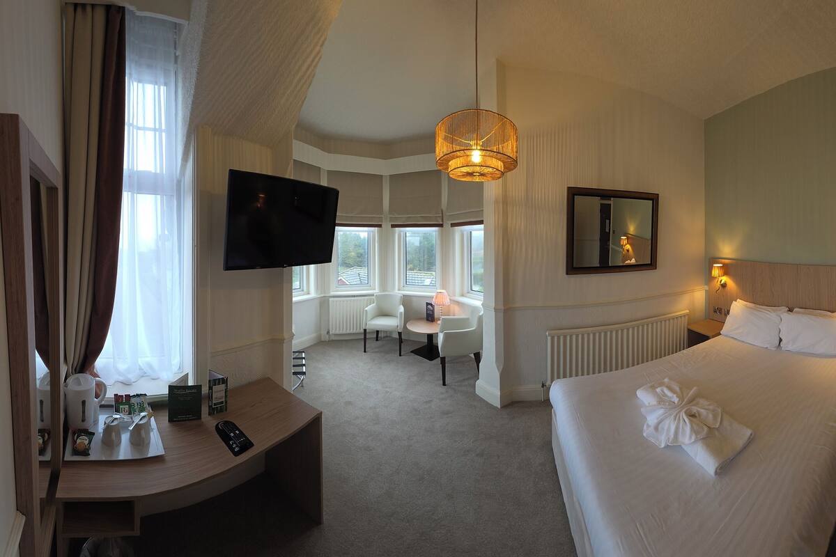 Ein Hotelzimmer mit Bett, Nachttisch, Fernseher und einer Sitzecke mit Tisch und Stühlen.