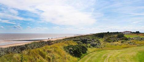 Eine Küstenlandschaft mit Strand, Wiesen und einem Haus in der Ferne.