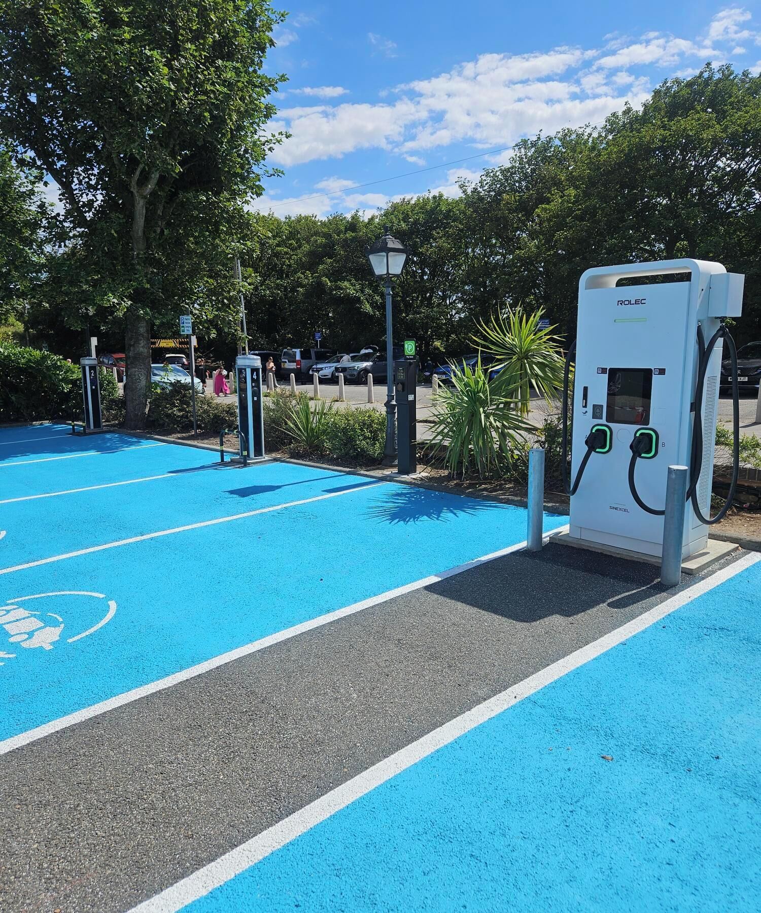 A parking area with electric vehicle charging stations, marked parking spaces, and a clear sky.