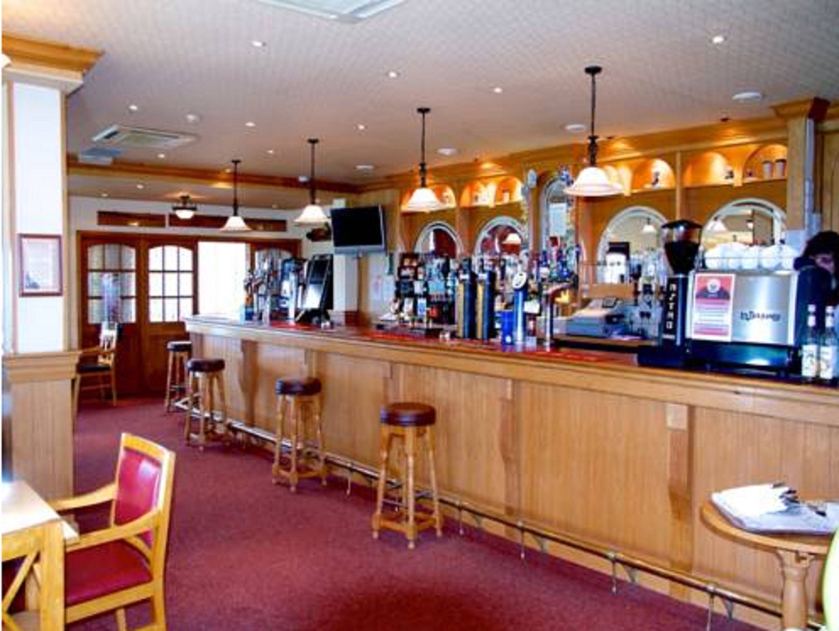 A bar area with wooden bar stools, a counter with a coffee machine, and a television mounted on the wall.