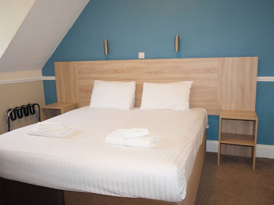 A neatly made bed with white linens and pillows, a wooden headboard, and two bedside tables with lamps.