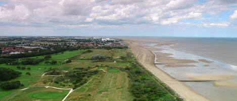 A coastal landscape with a beach, a golf course, and a town in the distance.
