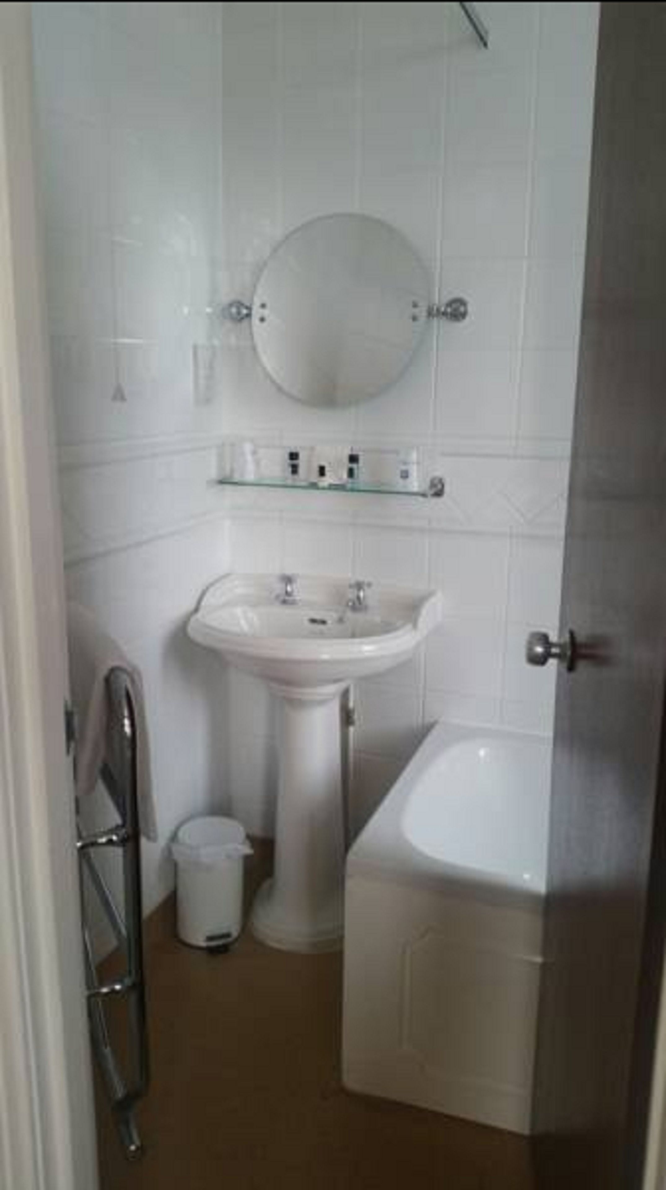 Un baño pequeño y blanco con lavamanos pedestal, un espejo encima y un inodoro.