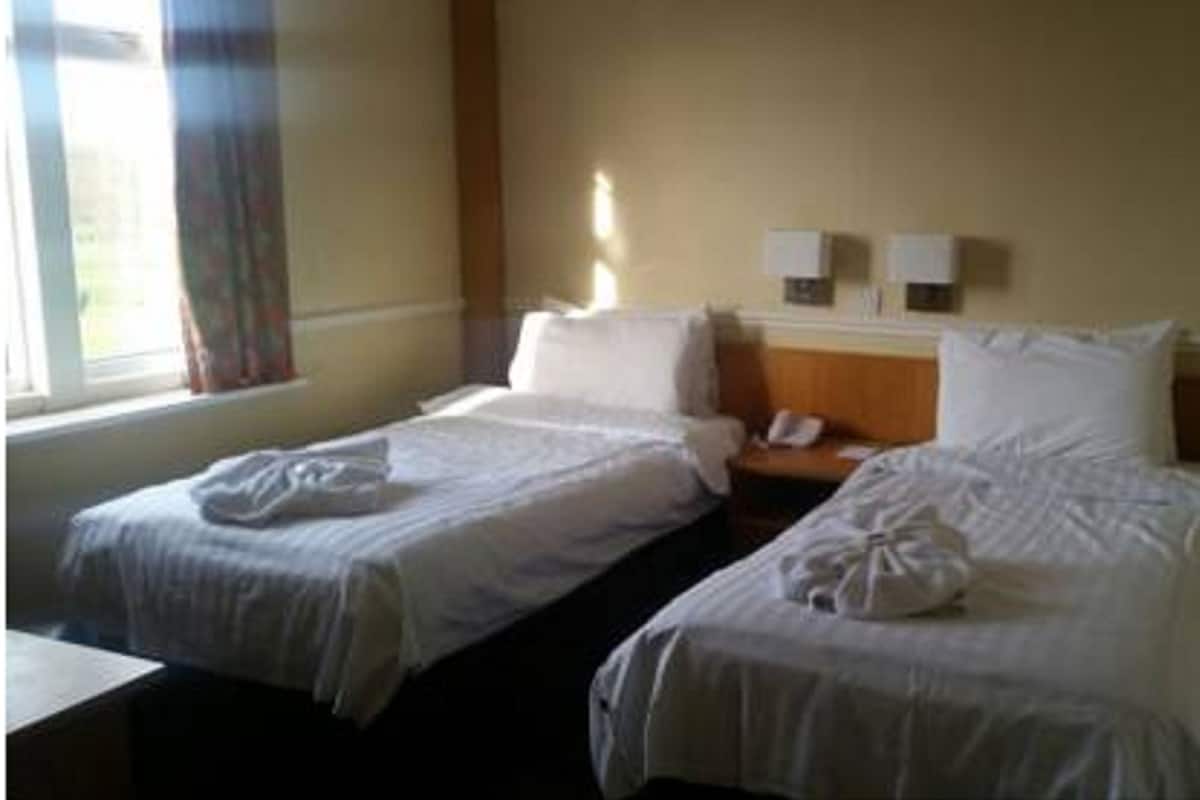 Ein Hotelzimmer mit zwei Betten, einem Nachttisch, einem Fenster mit Vorhängen und zwei Wandleuchten.