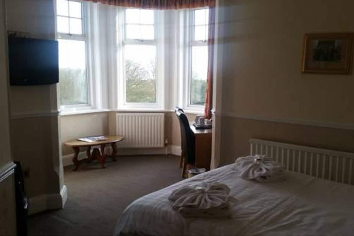 Ein Hotelzimmer mit Bett, Schreibtisch, Stuhl, Heizkörper und Fernseher an der Wand.