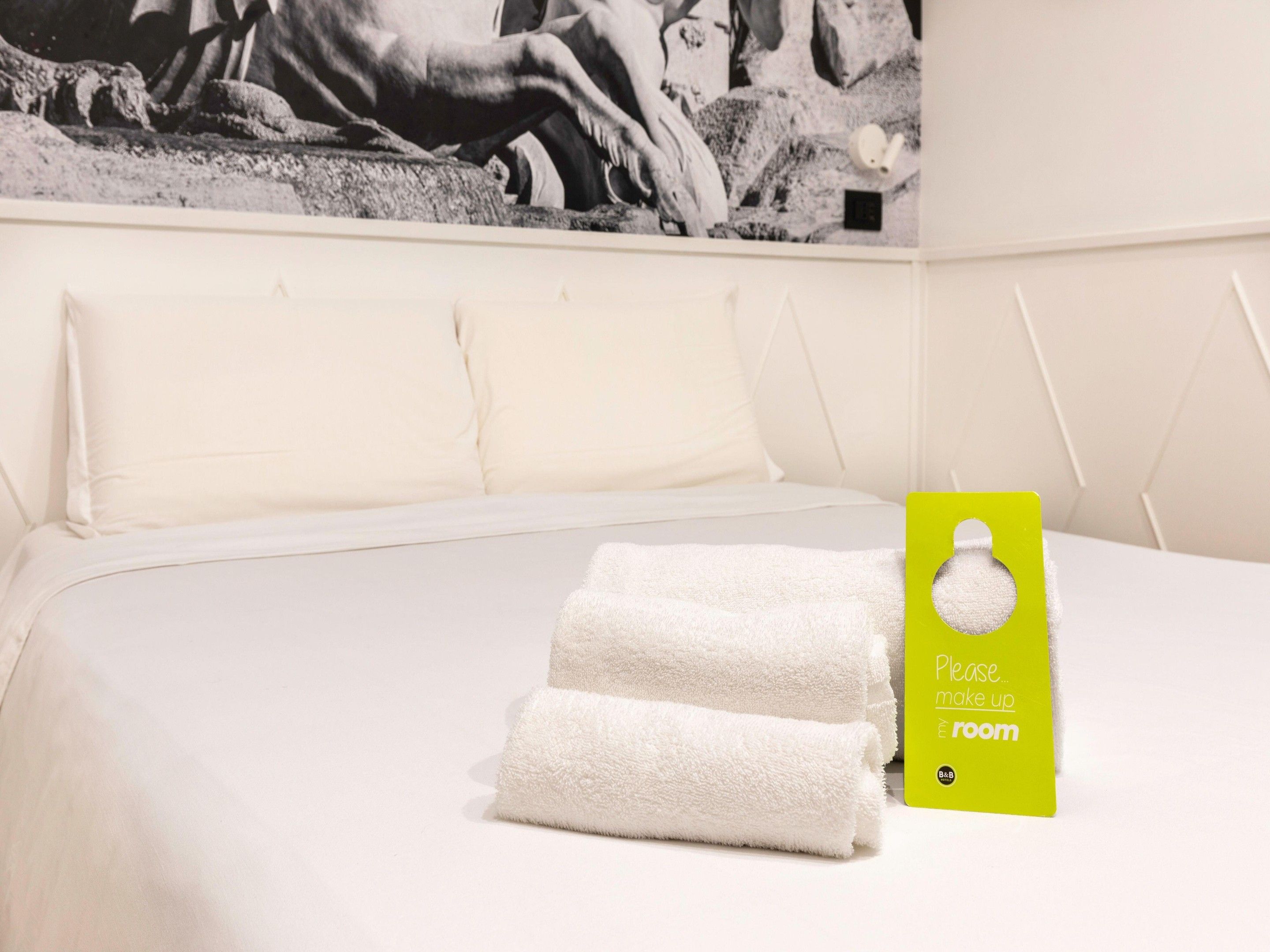 Una habitación de hotel con una cama bien hecha, ropa de cama blanca y un letrero verde en la pared.